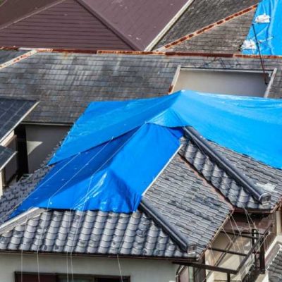 Houses with tiled roof covered by blue sheet after hurricane